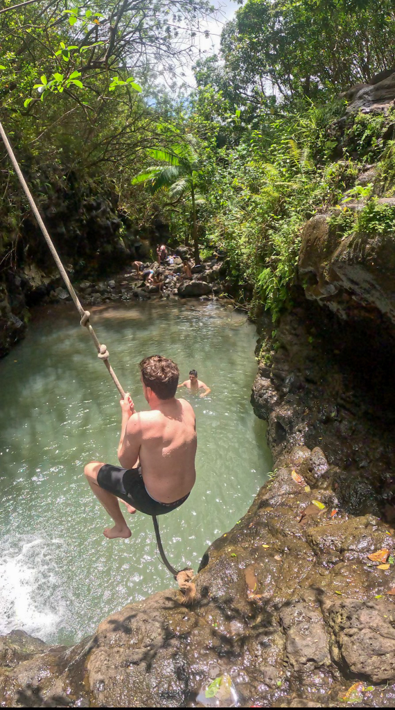 Person swinging on the rope swing into the swimming hole at Waimano Falls in Oahu